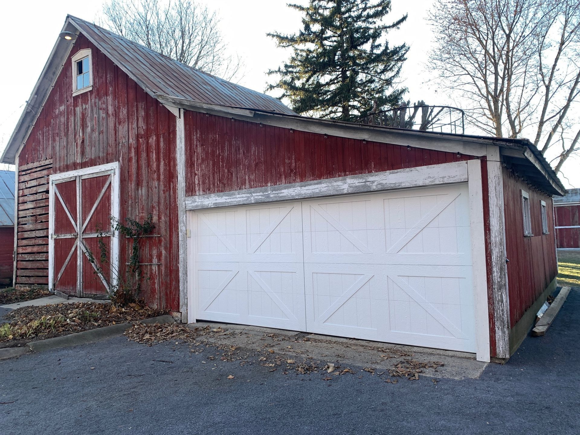 Red weathered barn with white garage door and double barn doors.