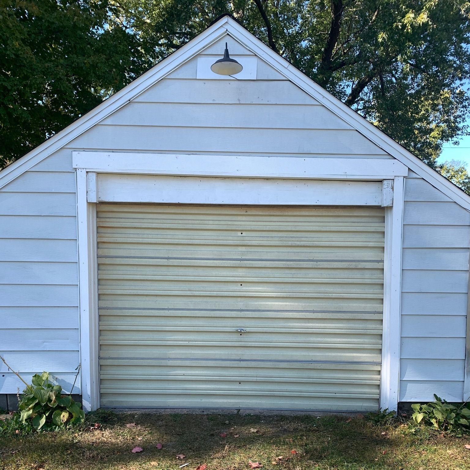 White garage with yellow door, surrounded by grass and plants, under a blue sky.