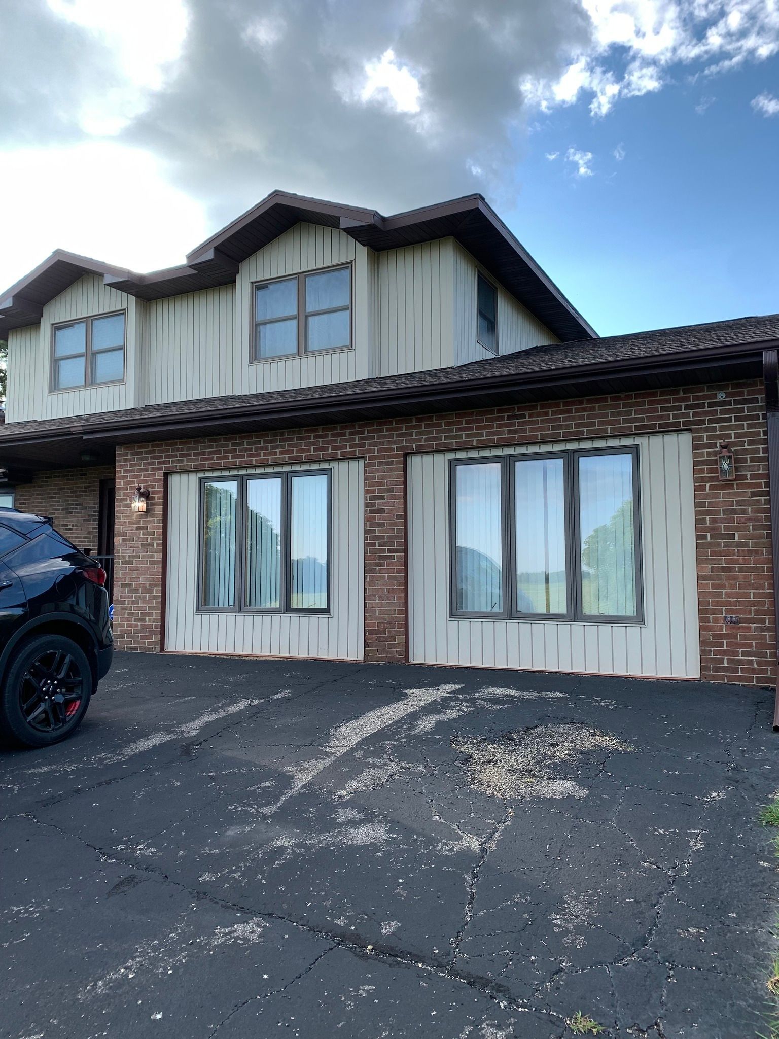 Two-story house with brick and tan siding. Black car parked in front. Blue sky.