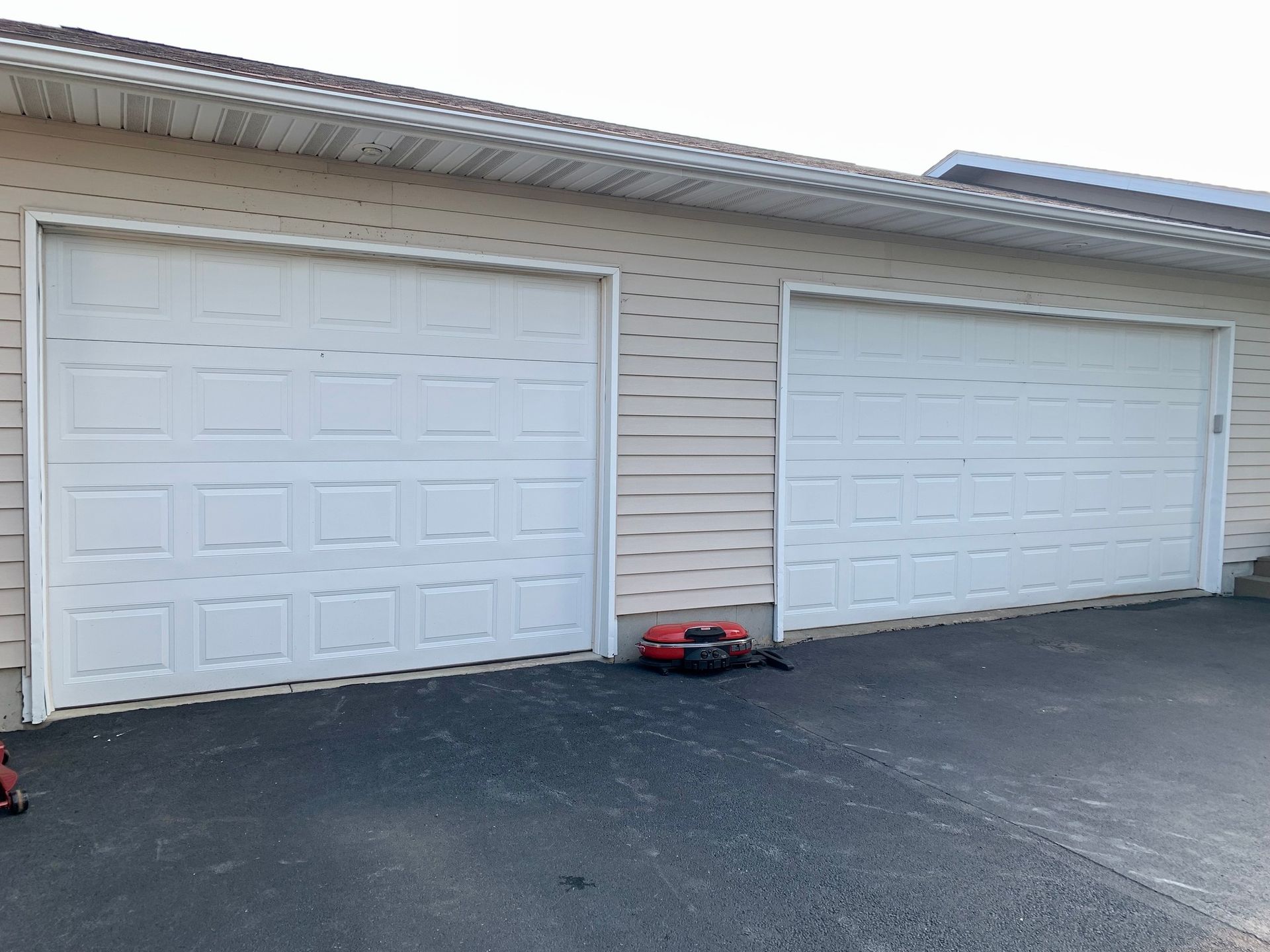 Two white garage doors on a beige house with black asphalt driveway.