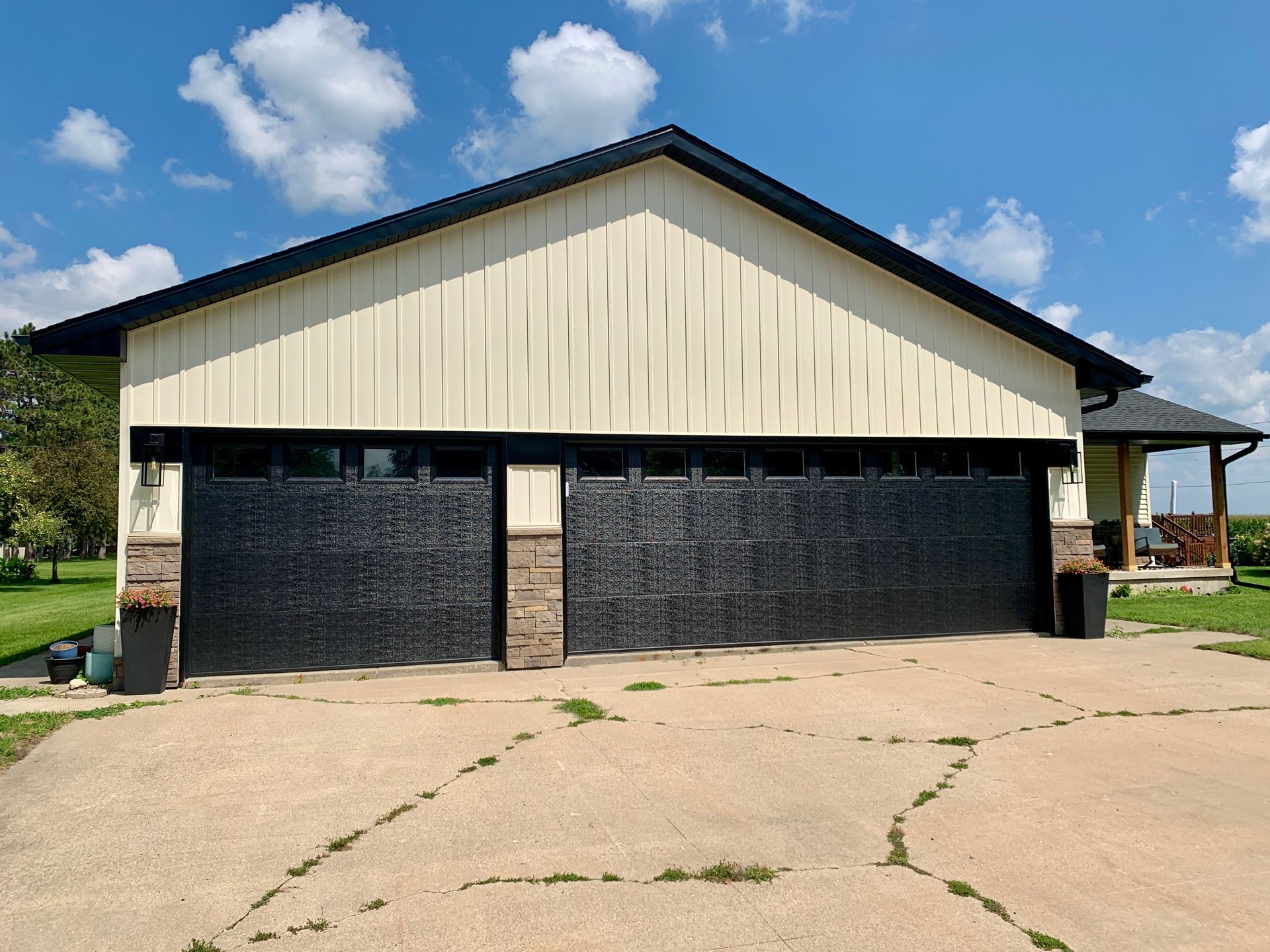 Garage with black doors, beige siding, and stone accents under a blue sky.