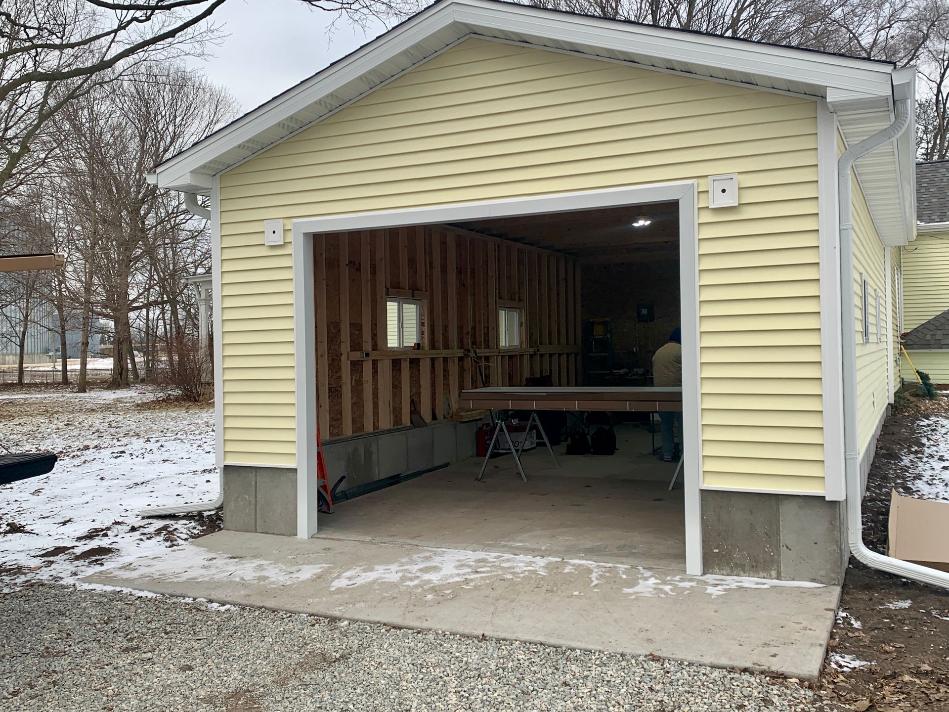 Yellow garage with open door, concrete pad, snow, and exposed interior framing.