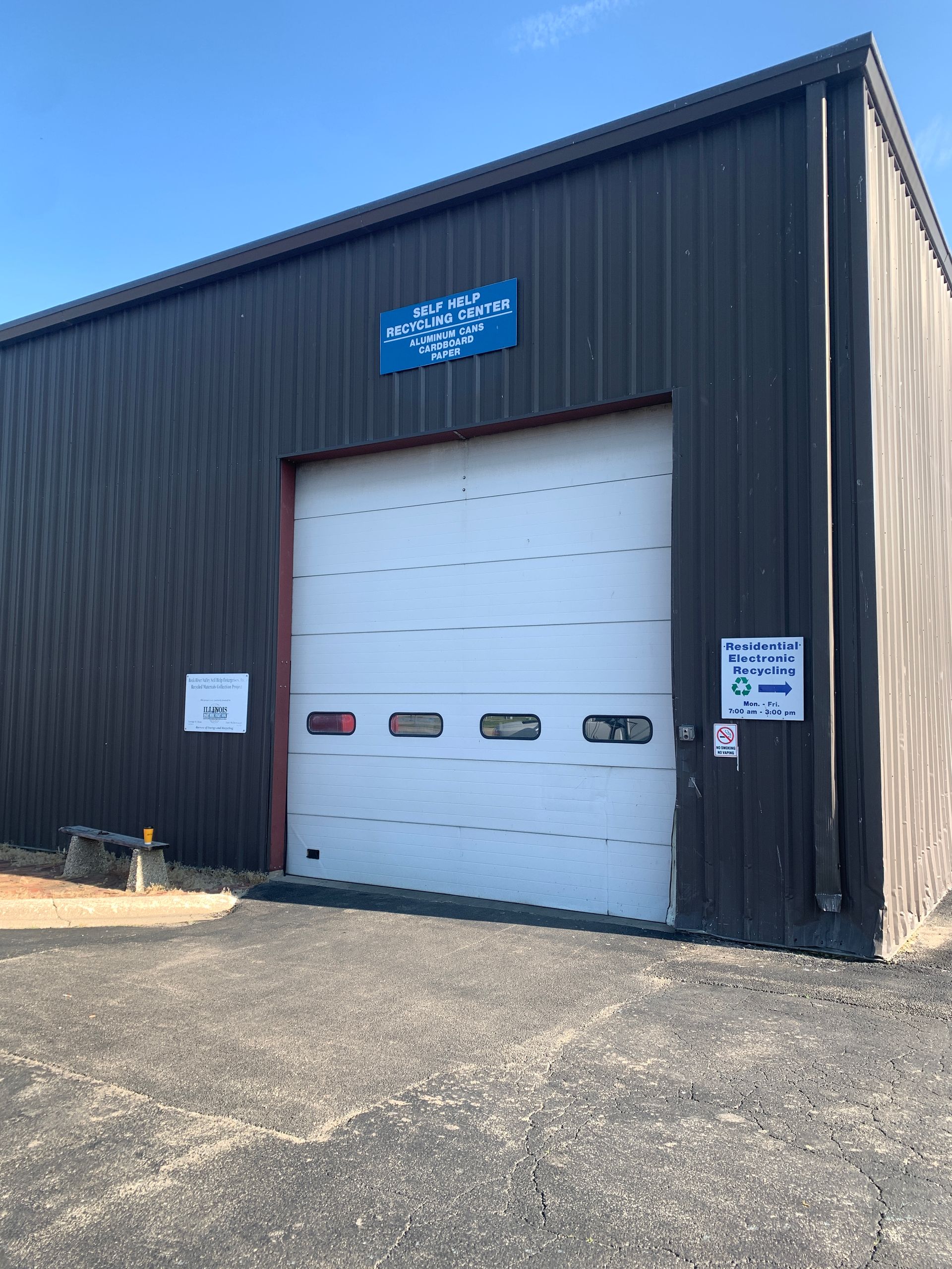 Dark metal building with a large white garage door; blue sign above the door.