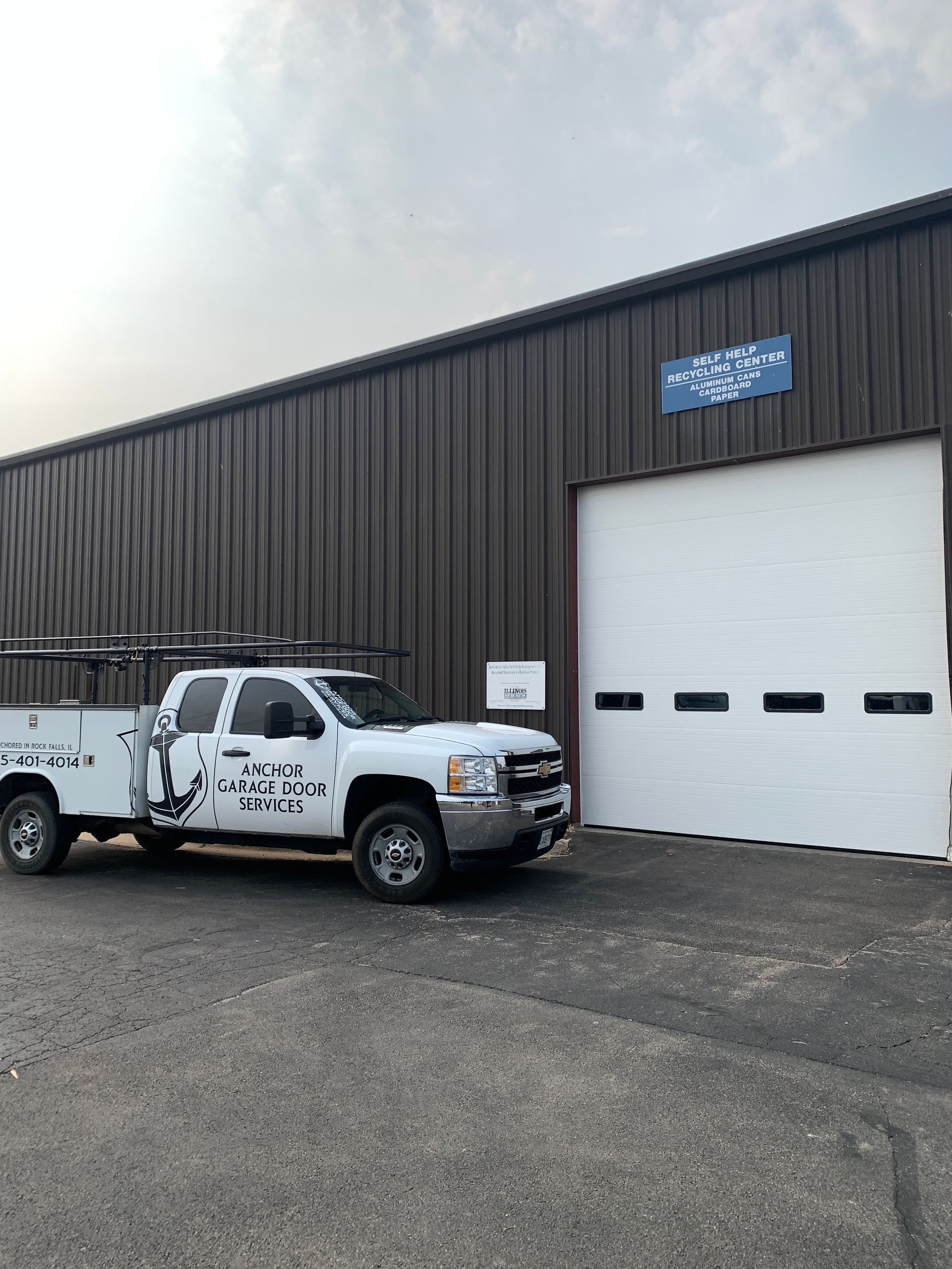 White work truck parked outside a brown metal building with a closed garage door.