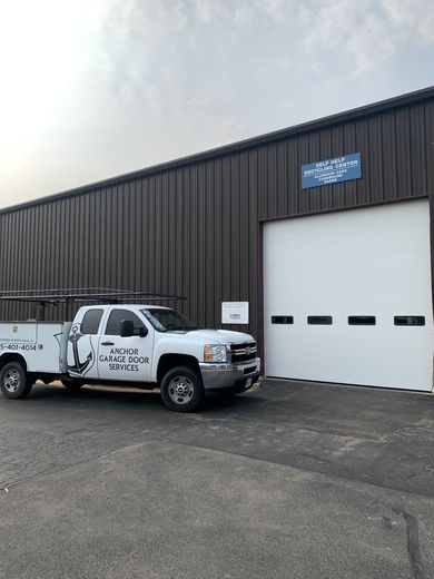 White truck with tools parked next to a dark gray industrial building with a closed garage door.