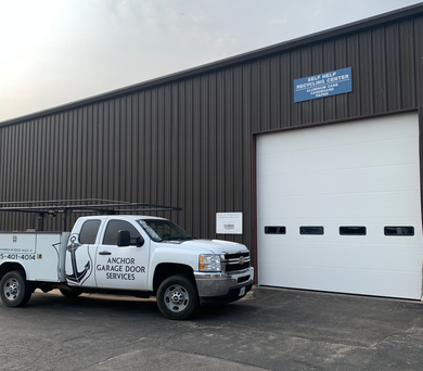 White truck with tools parked next to a dark gray industrial building with a closed garage door.
