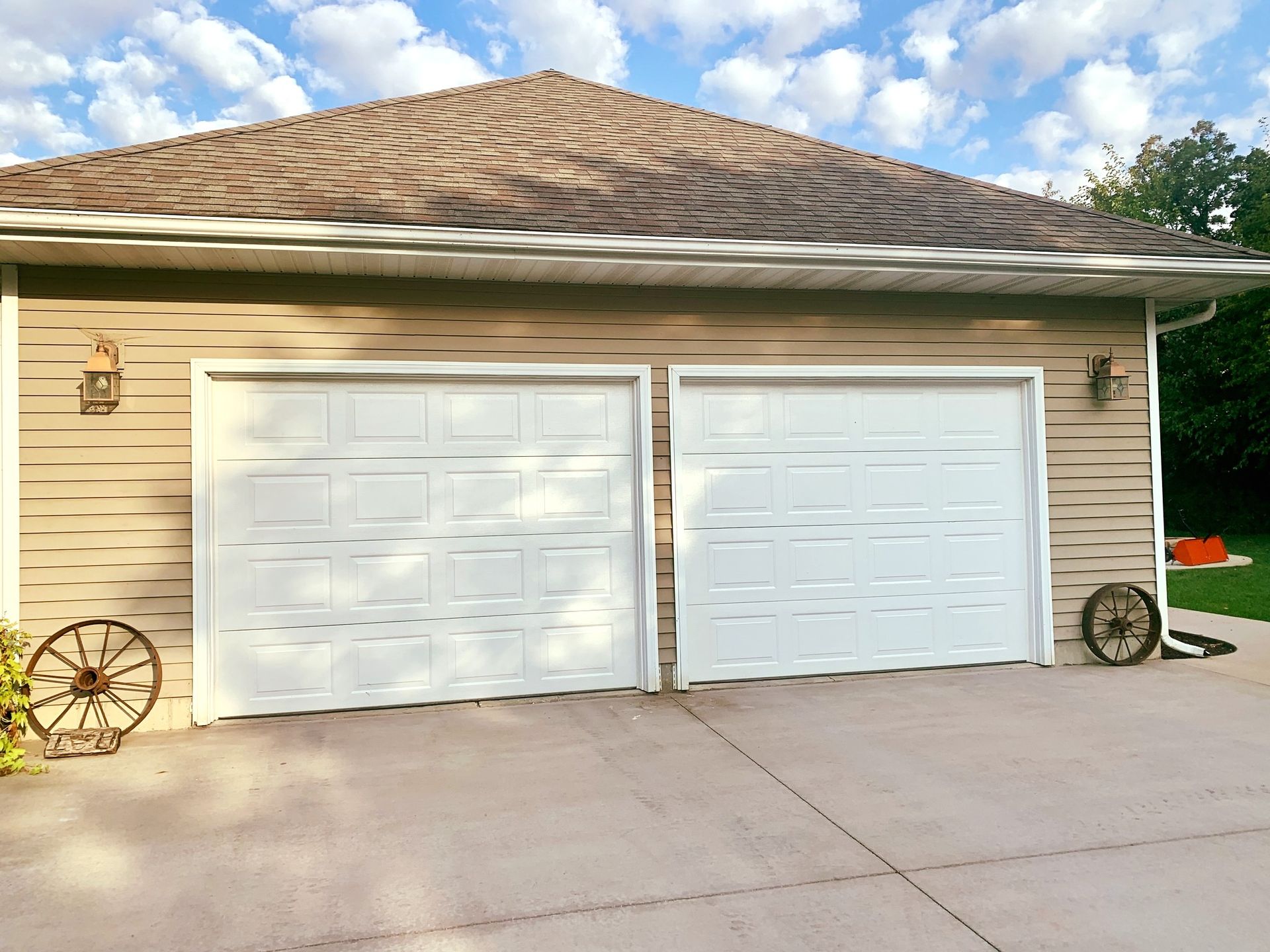 Two white garage doors with tan siding, brown roof, and a concrete driveway.