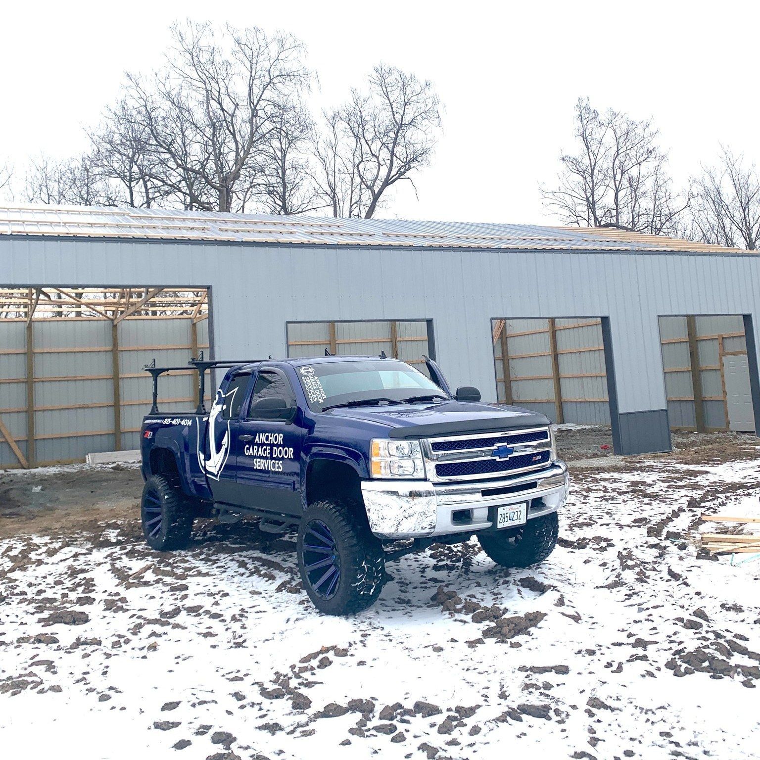 Dark blue Chevrolet pickup truck parked in front of a light gray building; snowy ground.