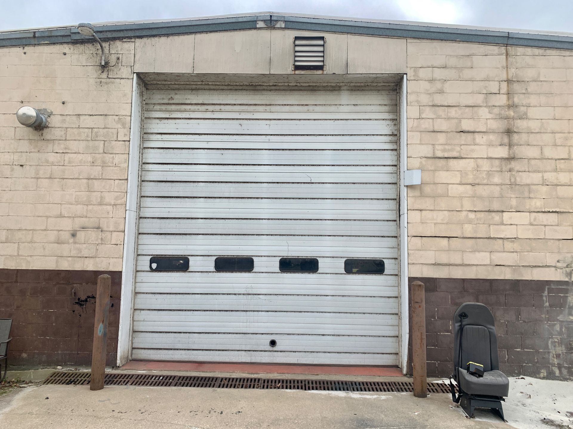 White industrial garage door on a light brown brick building, with an old chair on the side.
