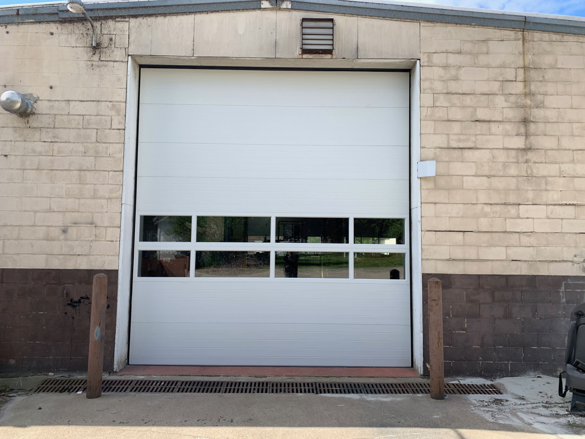 White garage door on a tan brick building with window panes; two brown poles in front.