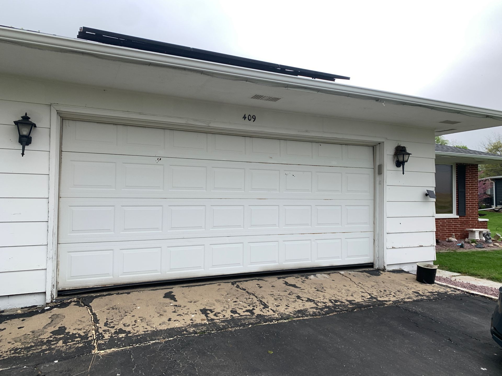 White garage with a closed door, two lights, and a cracked driveway.