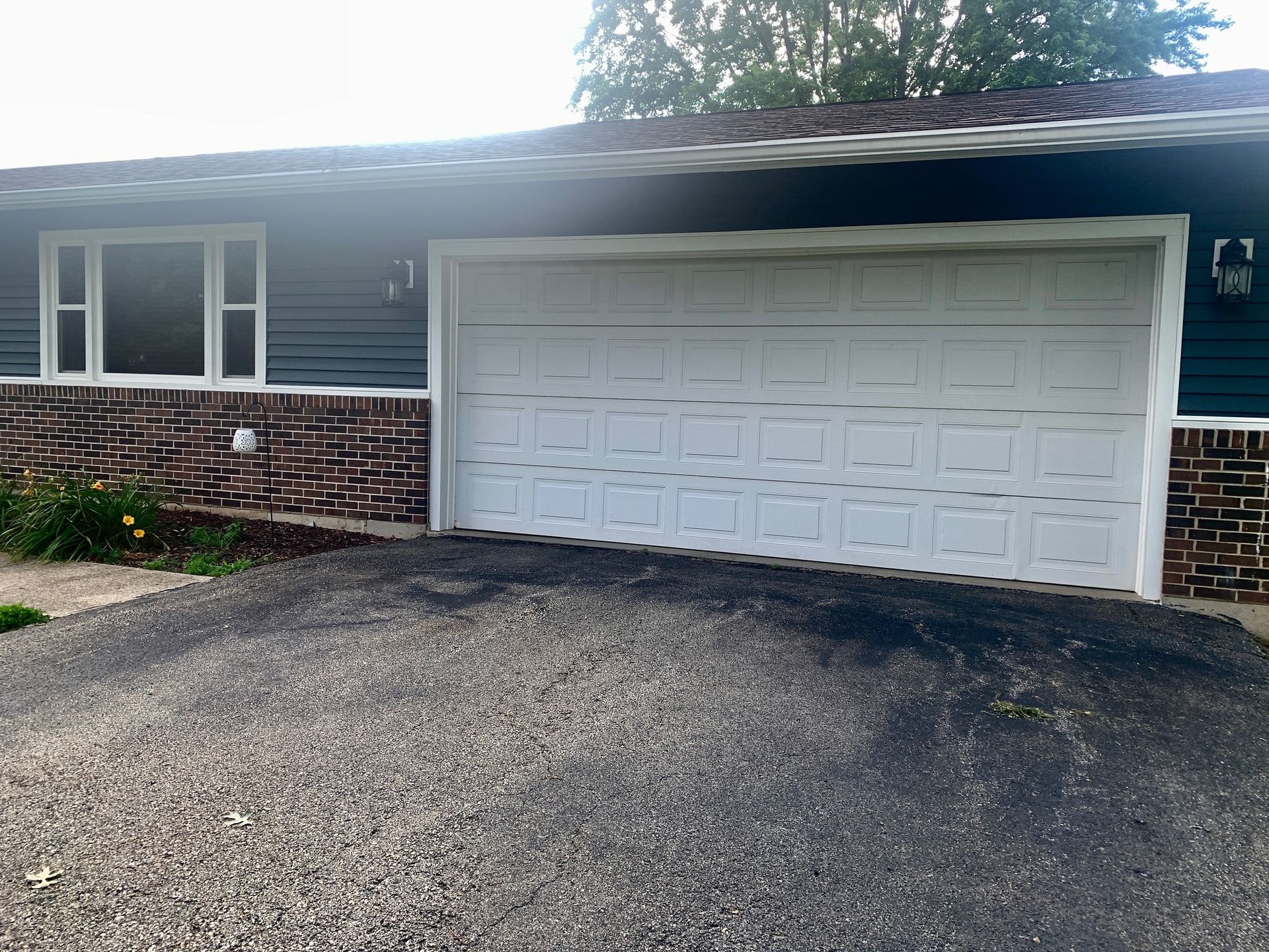 A house with a white garage door and a dark driveway; teal siding and brick accents.