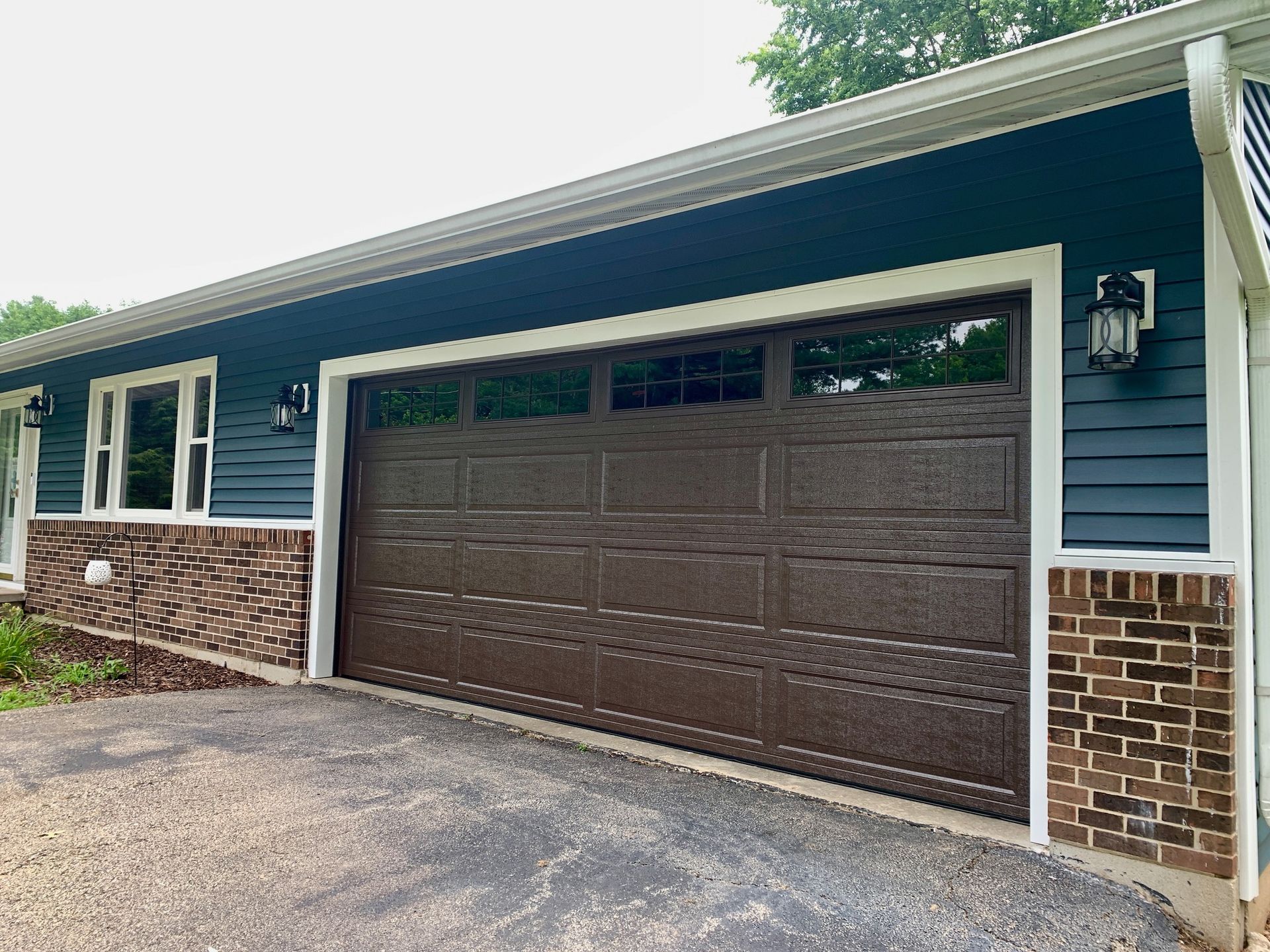 Brown garage door on a house with blue siding and brick accents.