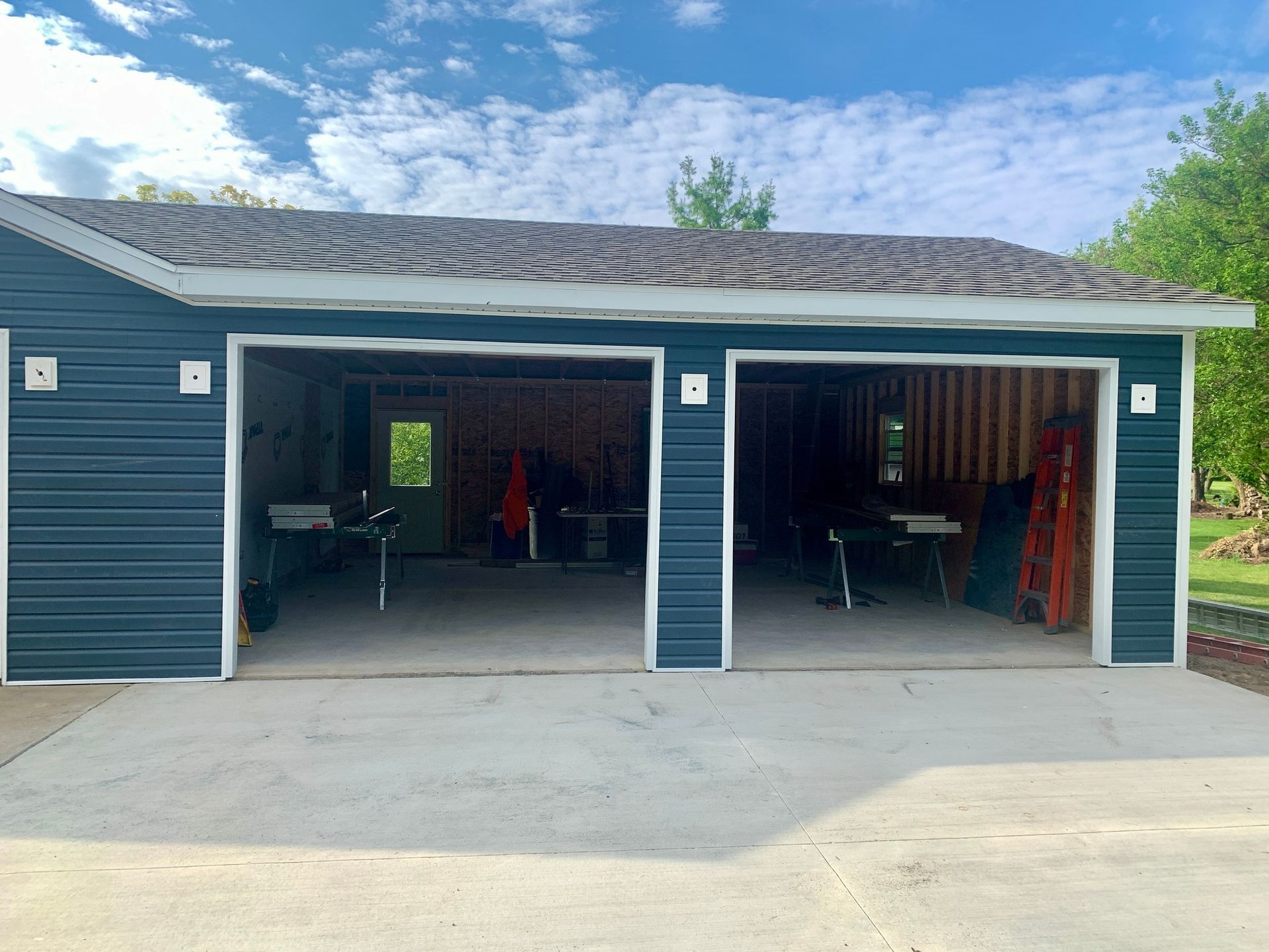 Blue garage with two bays, concrete floor, open doors, under cloudy blue sky.