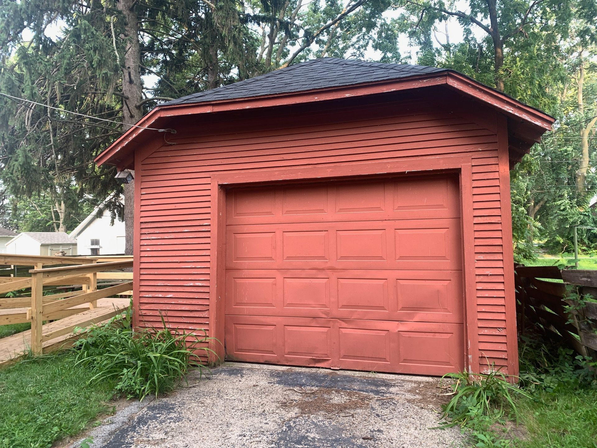 Red garage with black roof; driveway and wooden fence in front.