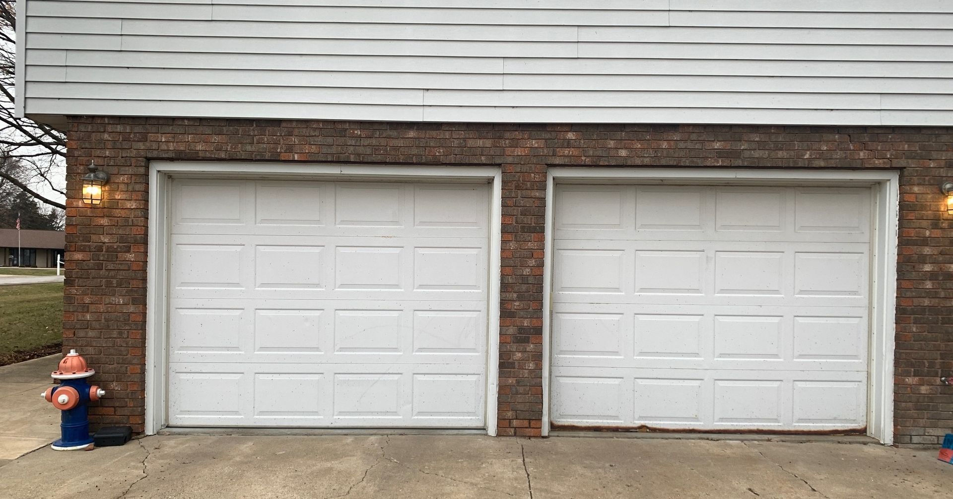 Two white garage doors in a brick-accented building, with a fire hydrant to the left.