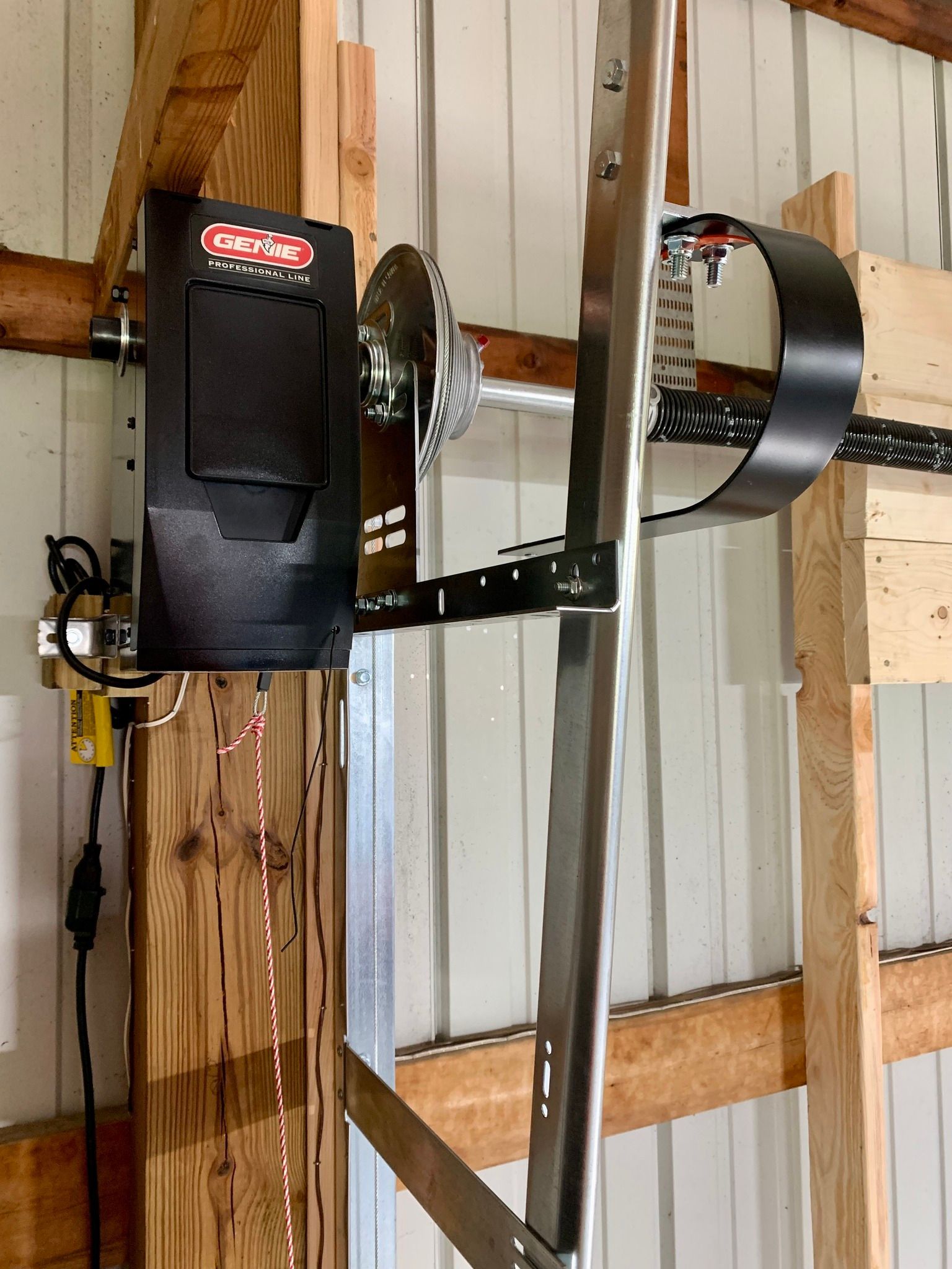 Garage door opener mounted on wooden beams, with a black motor unit and a chain drive.