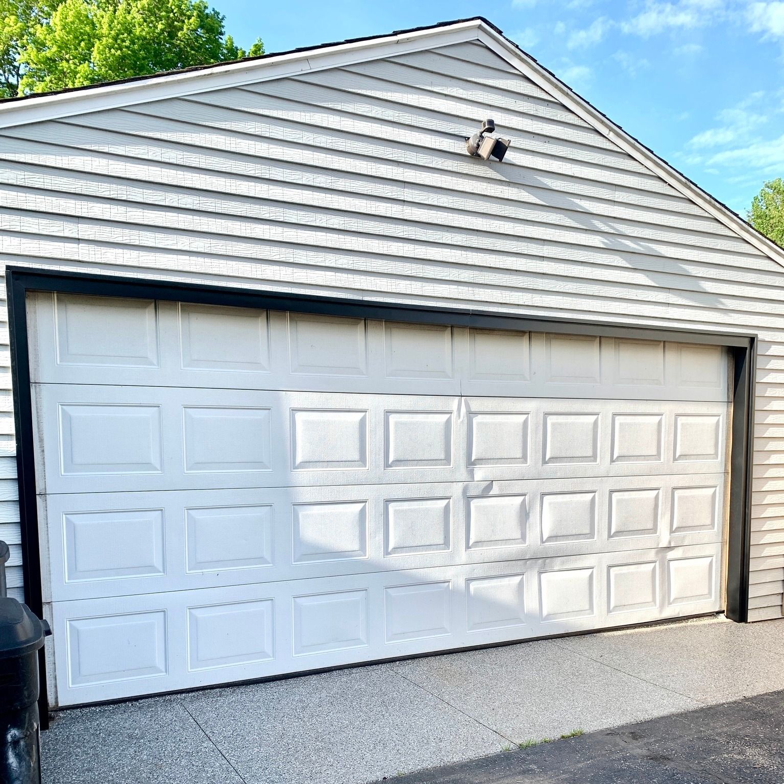 White garage door on a gray concrete driveway. White siding with black trim.