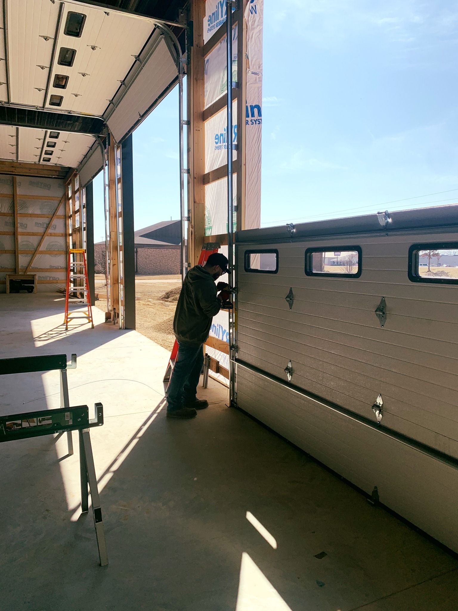 Construction worker installing a garage door, working outdoors on a sunny day.