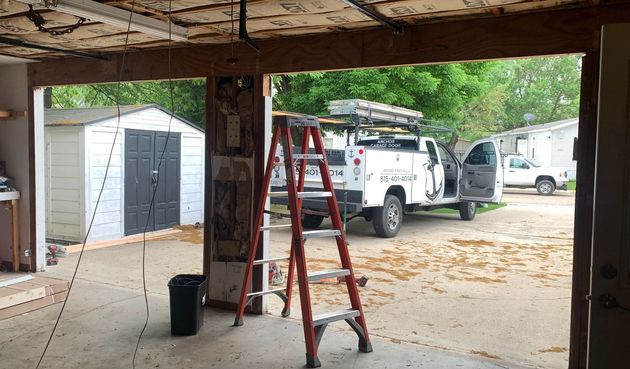 An open garage with a red ladder inside, a white truck parked, and a shed visible outside.