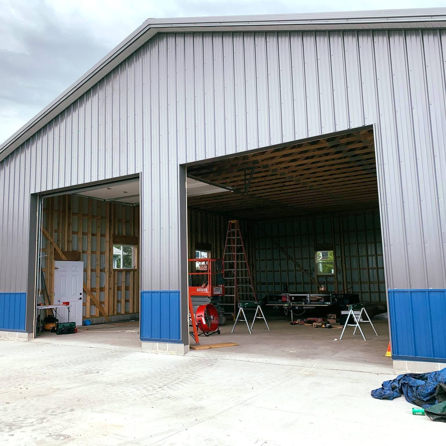 Large metal workshop with blue accents and open bays, construction in progress.