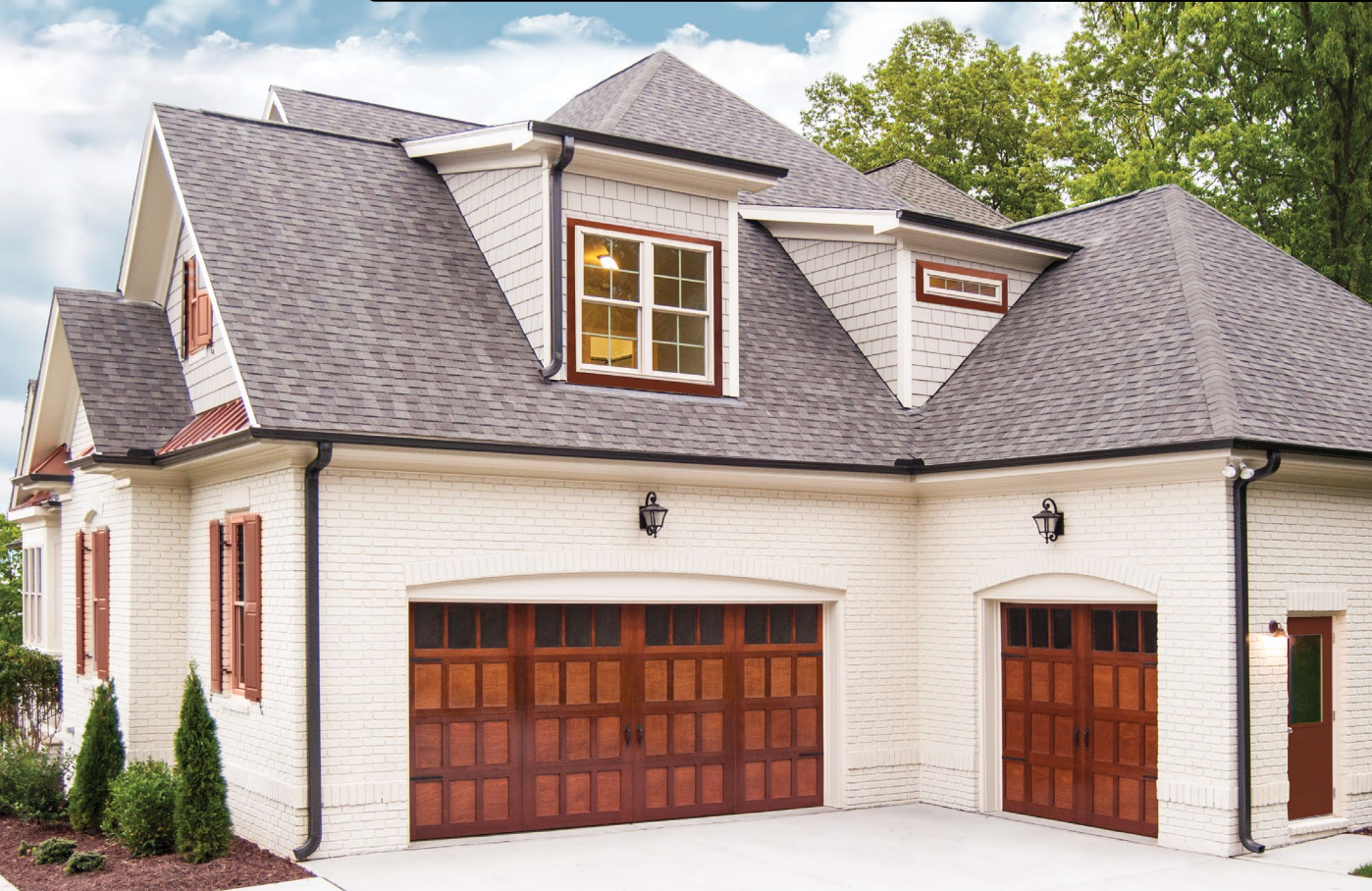 Two-car garage with brown doors and white brick exterior, gray roof, and small dormers.