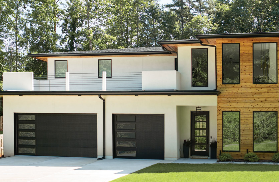 Modern two-story house with a black garage door, wooden siding, and large windows on a sunny day.