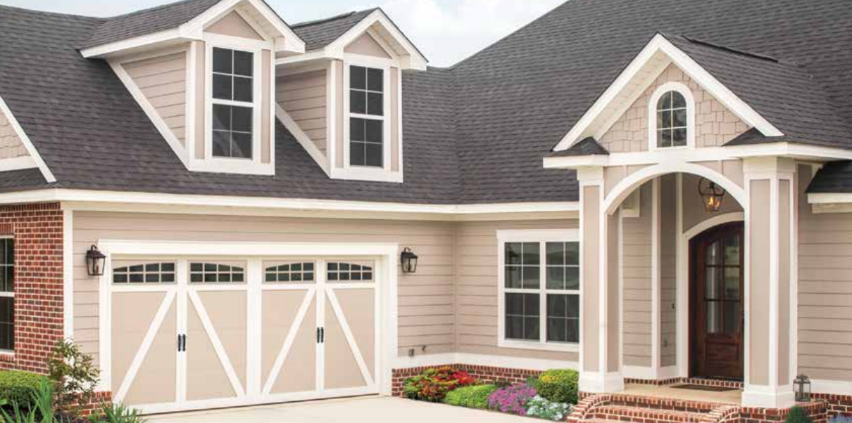 Tan house with black roof and white trim. Garage door with cross design and arched front entrance.