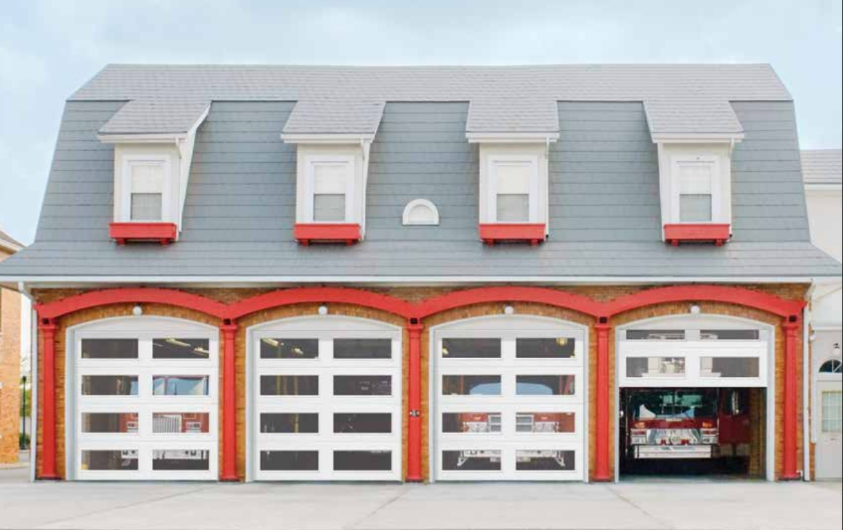 Fire station with gray mansard roof, red trim, and four garage doors, one open revealing a fire truck.