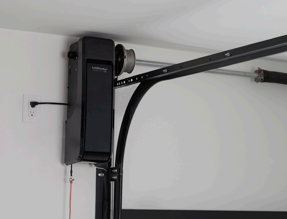 Garage door opener mounted on the ceiling, connected to the door track. Black and white, indoors.