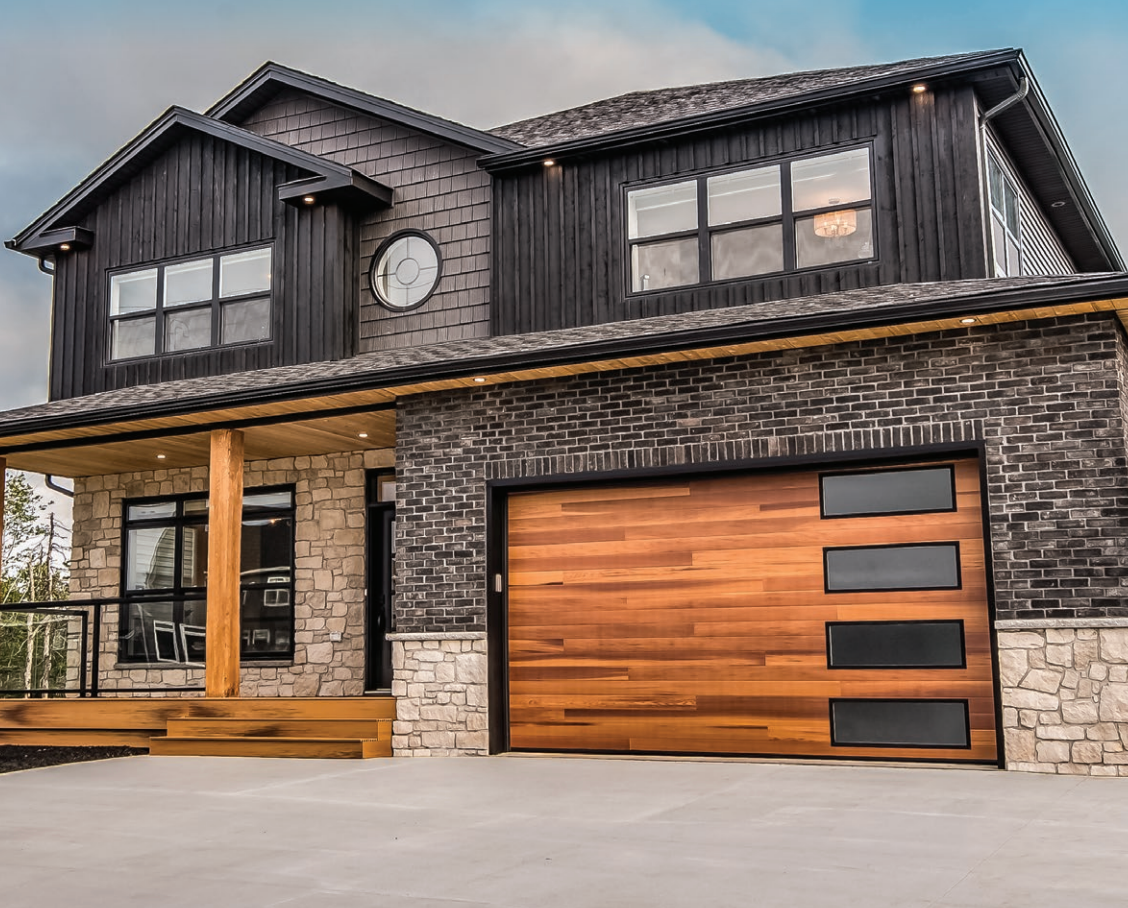 Two-story house with wooden garage door and brick facade. Features stone accents, black trim, and large windows.