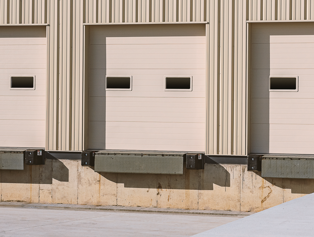 Loading docks on a beige building. Three doors with rectangular windows and textured bumpers.