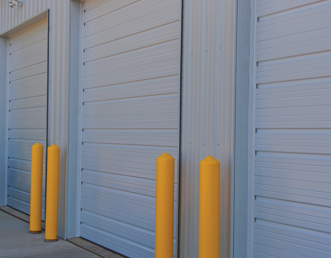 Three white storage unit doors with yellow bollards in front.