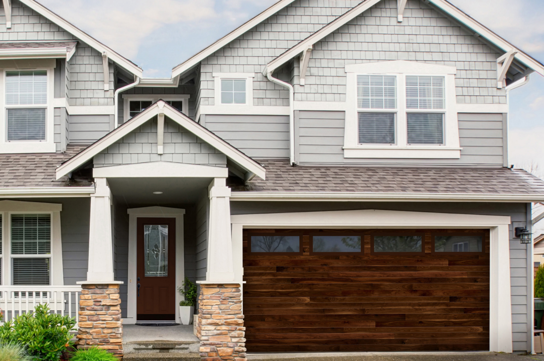 Two-story house with brown garage door and front door; gray siding and stone columns.
