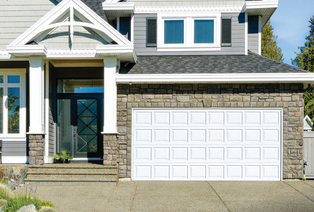 White garage door on a house with stone siding, entry with black door, gray roof.