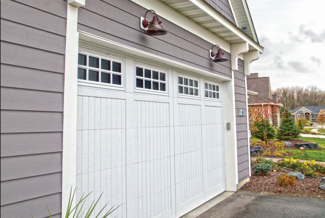 White garage door with window panels; gray siding, two bronze lights, and overcast sky.