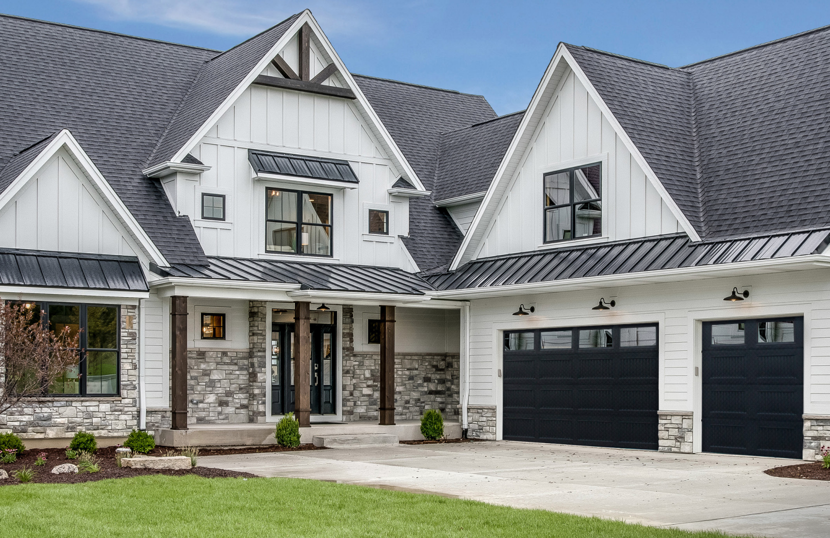 White house with black roof, stone accents, and black garage doors.