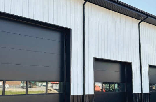 Black and white building with large garage doors. White vertical siding, black trim and doors.
