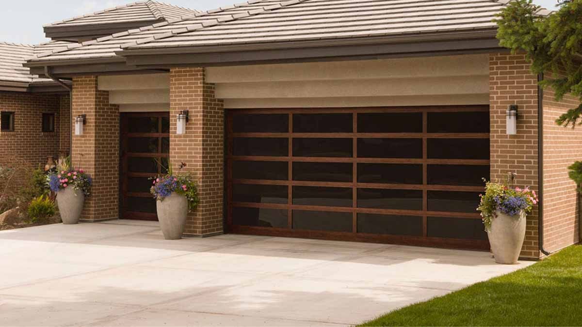 Three beige garage doors with small windows, flanked by stone columns and a metal roof.