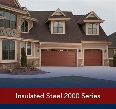 White garage door on a house with stone siding, entry with black door, gray roof.