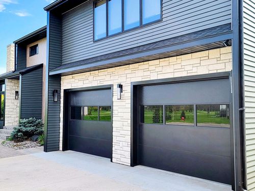 White garage door on a white house with a brown roof and surrounding bushes.