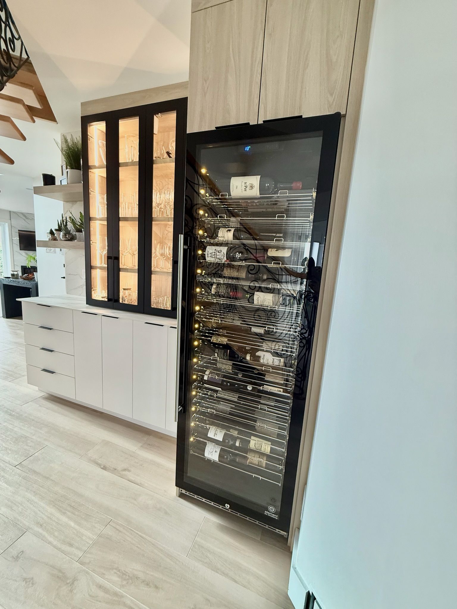 Cave à vin encastrée avec porte vitrée, à côté d'un meuble à portes ouvertes dans une maison moderne.