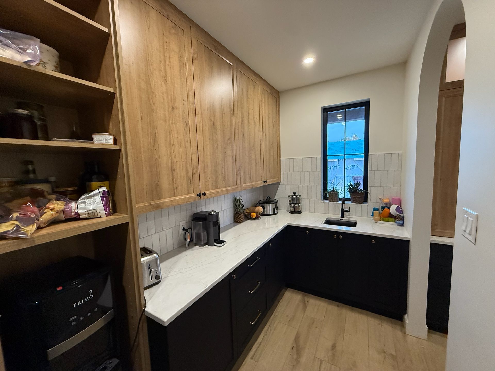 Garde-manger avec placards et plans de travail en bois. Meubles bas noirs, fenêtre avec vue et étagères intégrées.