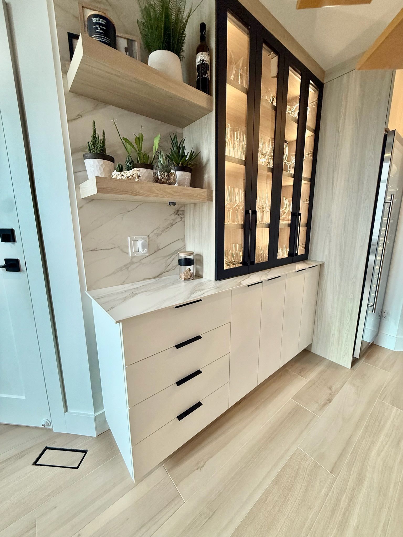 Bar intégré avec meuble vitré, tiroirs, étagères et plantes, dans une cuisine moderne avec parquet.