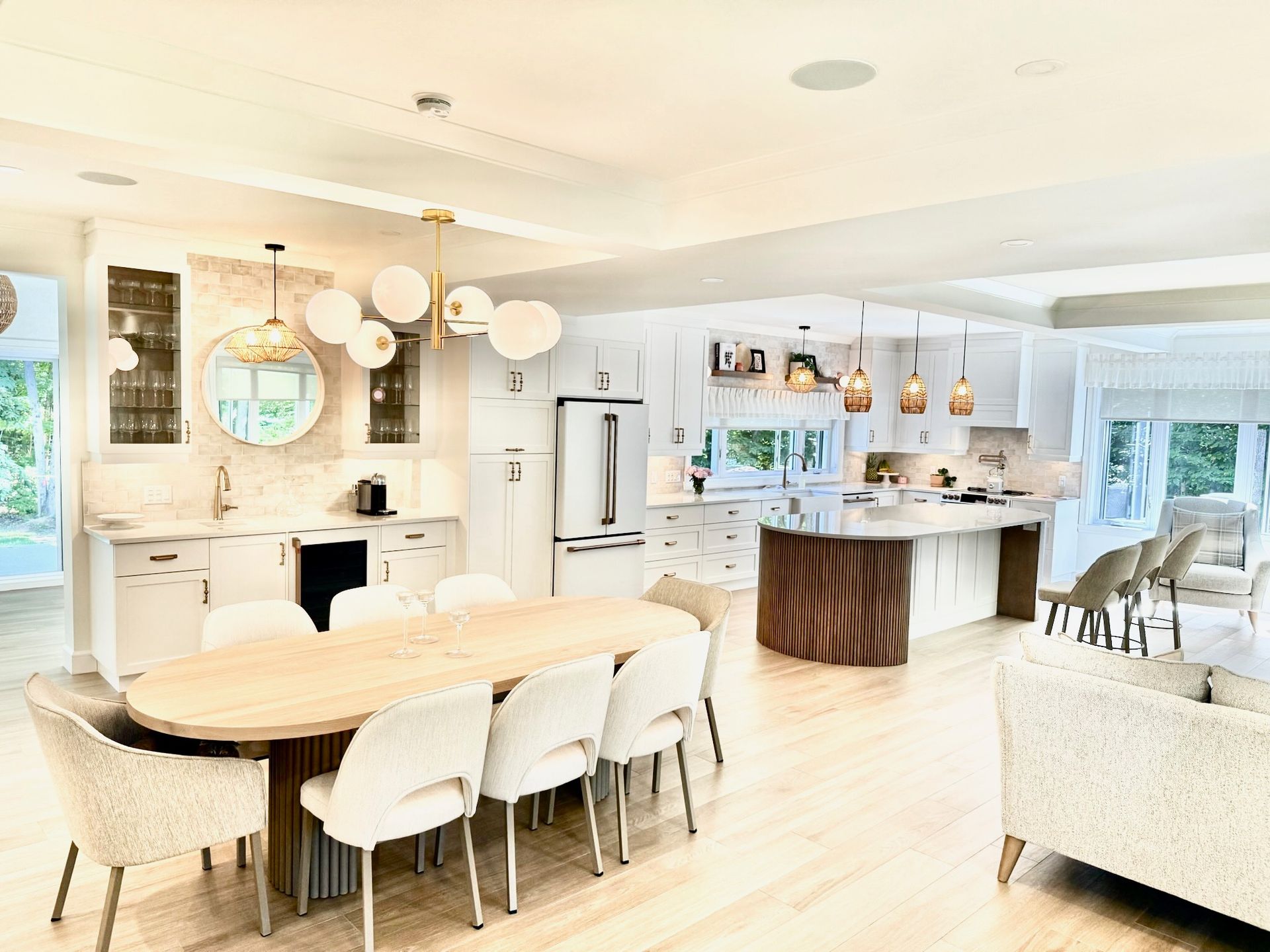 Cuisine et salle à manger à aire ouverte avec armoires blanches, table en bois et luminaires dorés.