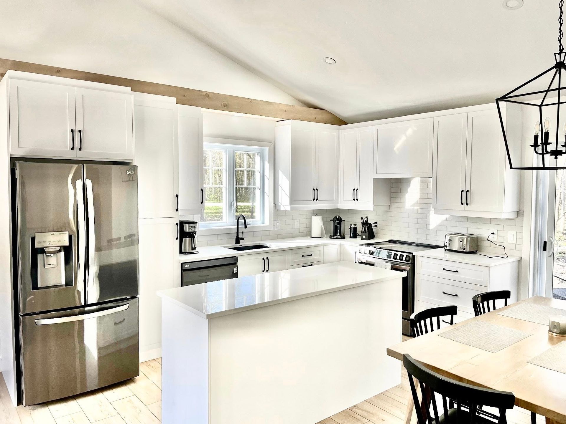 Cuisine moderne et lumineuse avec armoires blanches, réfrigérateur en acier inoxydable et îlot central.