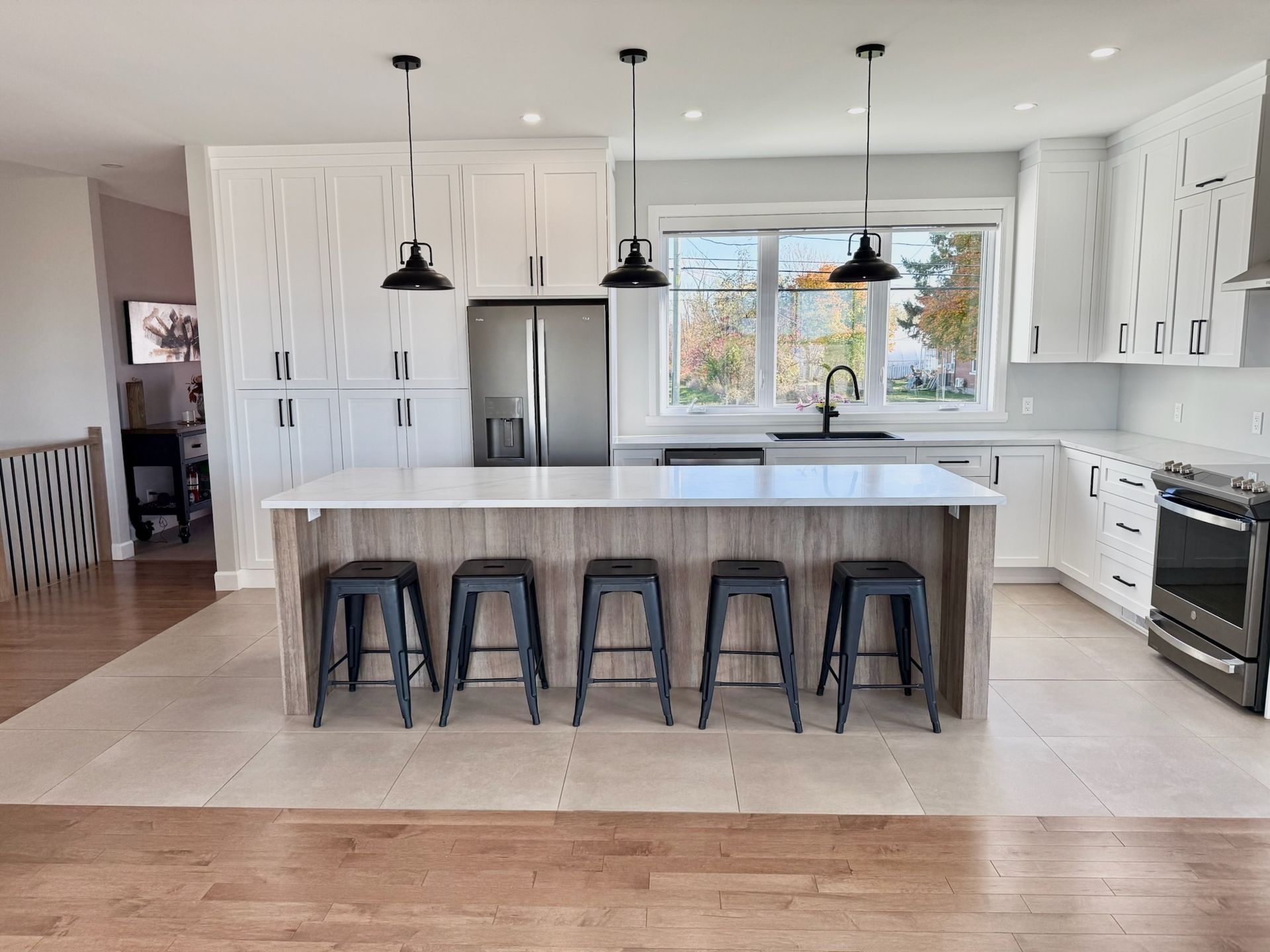 Cuisine moderne avec placards blancs, îlot central avec tabourets et trois suspensions lumineuses.