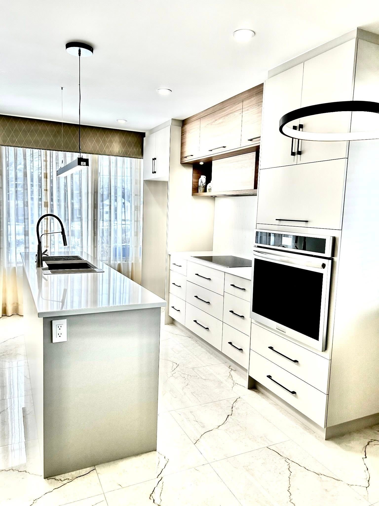 Cuisine moderne blanche avec îlot central, robinet noir et four en acier inoxydable.