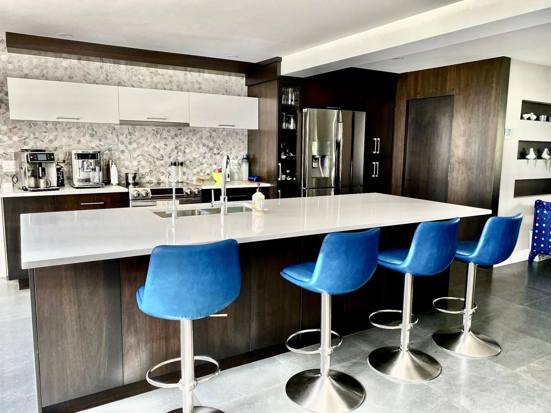 Cuisine moderne avec comptoir blanc, tabourets de bar bleus et appareils électroménagers en acier inoxydable.