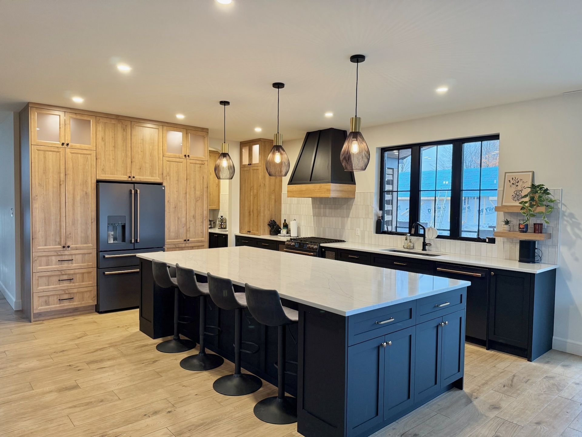 Cuisine moderne avec îlot et placards noirs, placards en bois clair et plan de travail blanc.